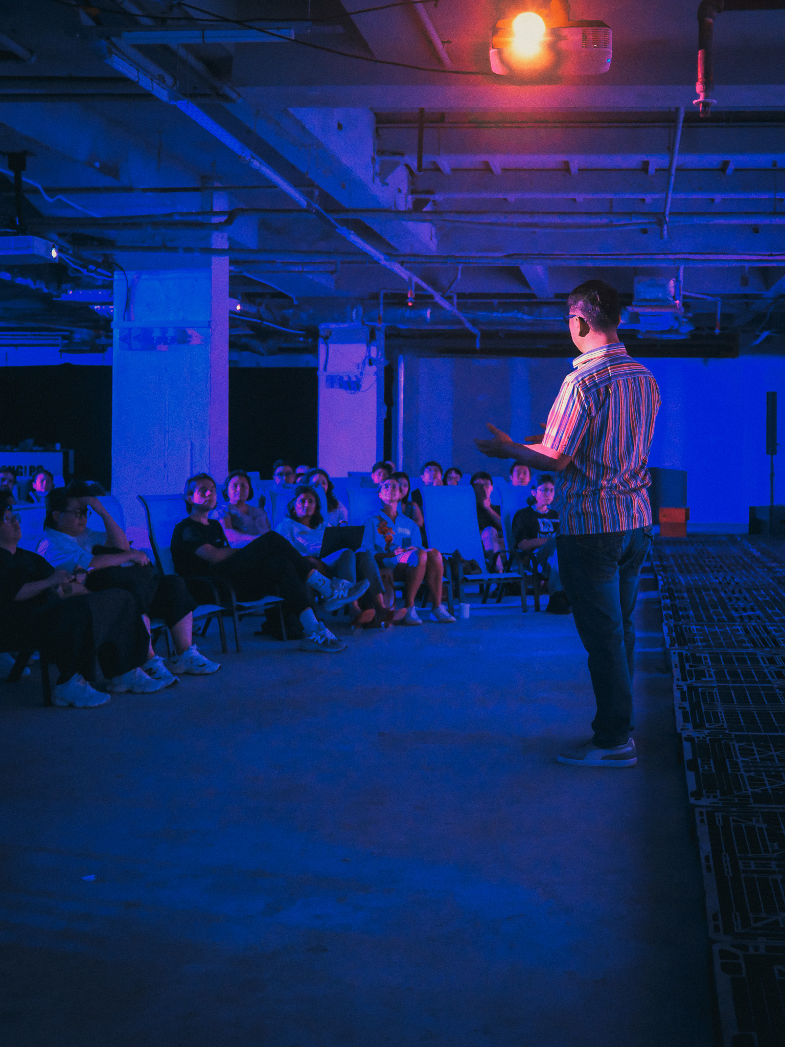 A speaker addressing an audience under blue lighting