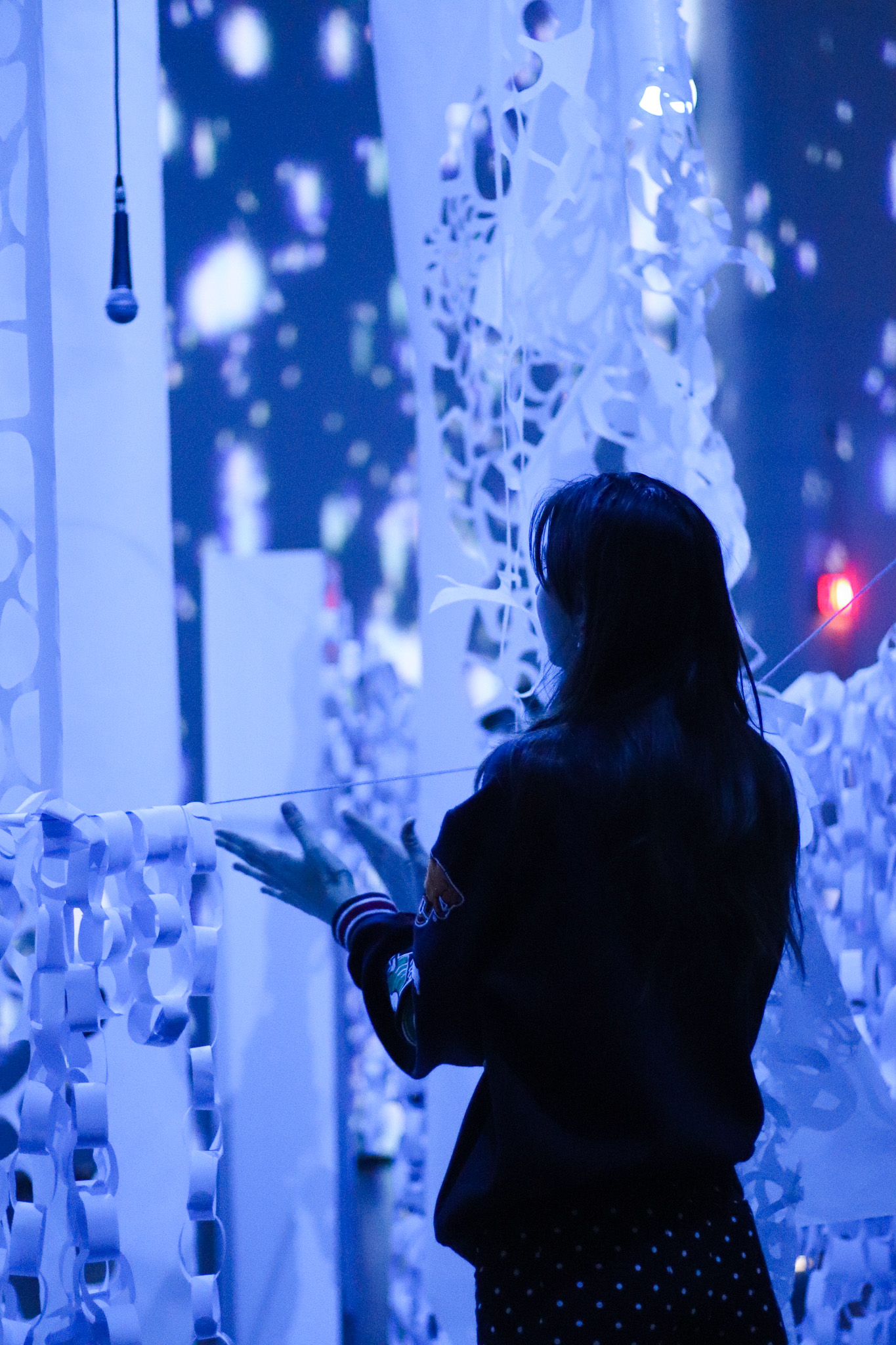 A visitor interacting with a blue-lit paper installation